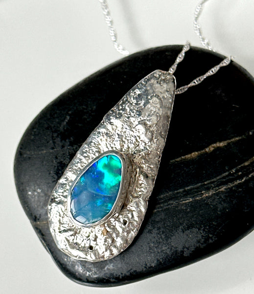 Lightning Ridge opal pendant necklace showcased on a textured silver setting over a smooth black stone.