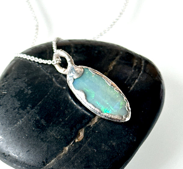 Solid Mintabie Opal in a silver pendant necklace, featuring vibrant blue flashes, on a stone backdrop.