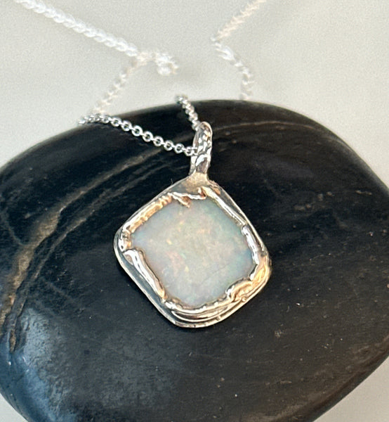 Coober Pedy opal pendant necklace featuring a pale blue opal with neon colors, set in a textured copper and silver design.