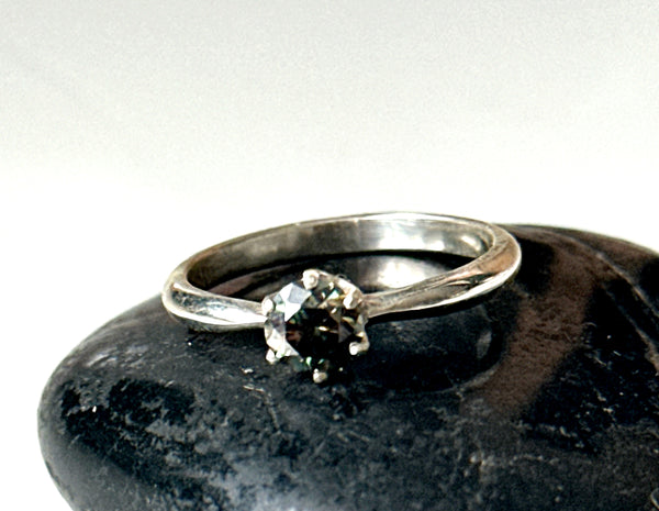 Moissanite solitaire silver ring featuring a faceted Moissanite on a sterling silver prong shank resting on a black stone.