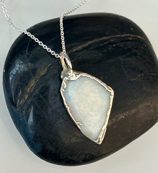 Coober Pedy opal silver pendant necklace resting on a smooth black stone, showcasing its unique pale blue tones.