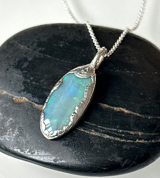 Solid Mintabie opal silver pendant necklace on a dark stone background showing vibrant blue and green flashes.