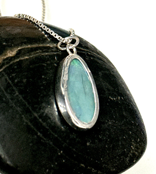 Mintabie opal sterling silver pendant necklace showcasing a blue opal on a silver chain, laid on a dark stone surface.