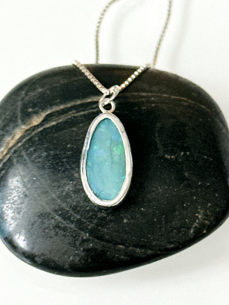 Mintabie opal sterling silver pendant necklace resting on a dark stone surface, showcasing its unique colors.