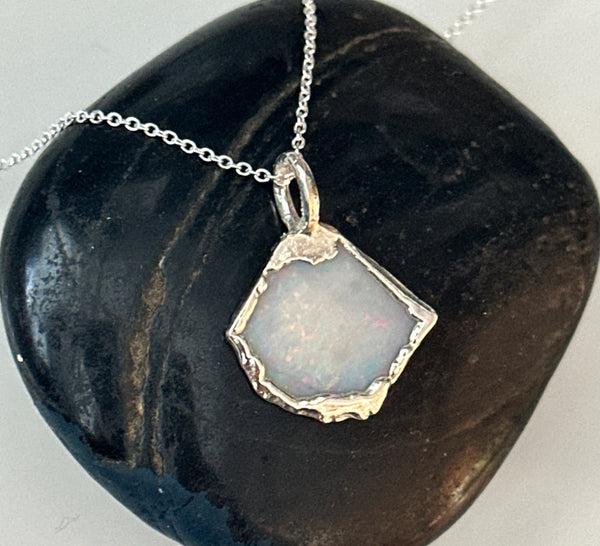 Coober Pedy opal silver pendant necklace showcasing pale blue opal set in textured silver on a black stone background.