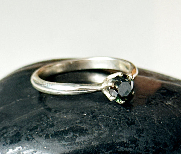 Moissanite solitaire silver ring on a dark stone background, showcasing the beautiful green/golden tone of the stone.