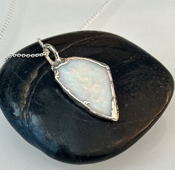 Coober Pedy opal silver pendant necklace on a smooth black stone, showcasing the unique opal colors.