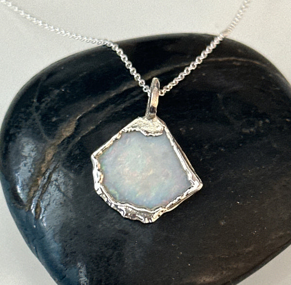 Coober Pedy opal set in a textured silver pendant necklace, showcasing a pale blue tone with neon colors.