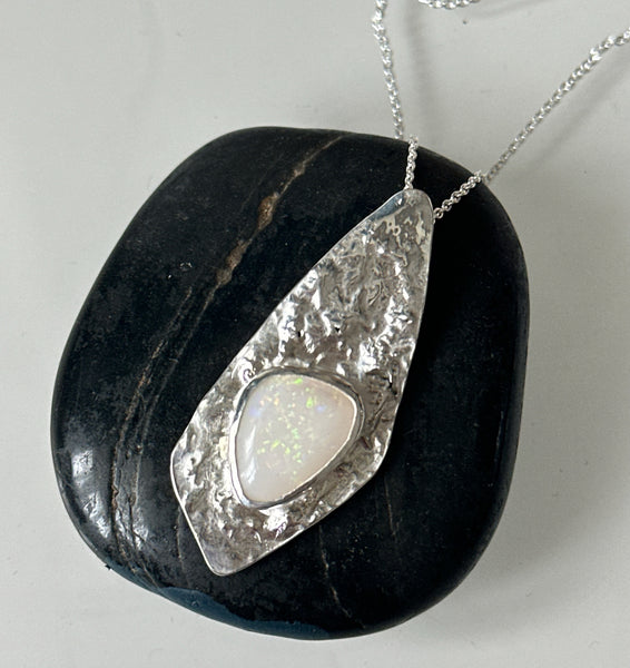 Coober Pedy opal silver necklace displayed on a smooth black stone background, showcasing its unique design and shimmer.
