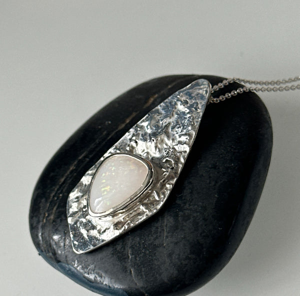 Coober Pedy opal silver necklace displayed on a smooth black stone with a unique textured pendant.