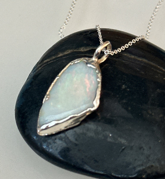 Coober Pedy opal silver pendant necklace displayed on a black stone surface, showcasing its unique pale blue tones.