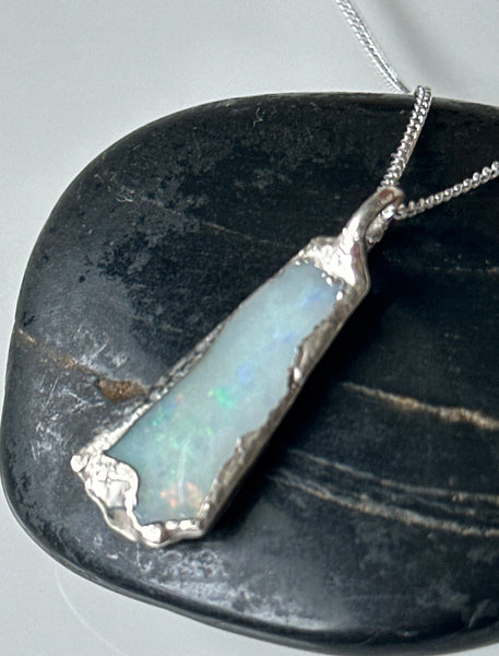 Solid Coober Pedy opal silver pendant necklace with neon rainbow flashes displayed on a dark stone backdrop.