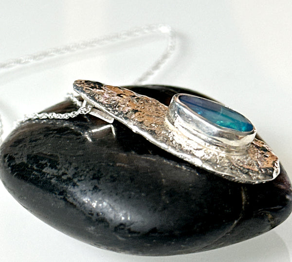 Lightning Ridge opal pendant necklace resting on a smooth black stone, showcasing its unique reticulated silver design.