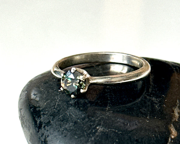 Moissanite solitaire silver ring featuring a faceted Moissanite stone set in sterling silver on a black stone.