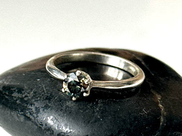 Moissanite solitaire silver ring with a faceted green/golden stone set in sterling silver on a black stone surface.