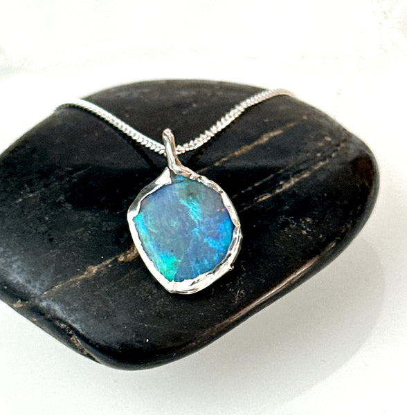 Lightning Ridge Opal pendant necklace on a black stone, showcasing vibrant blue and green tones with a silver setting.
